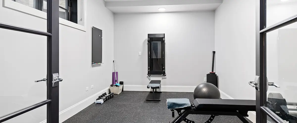 Home gym in basement remodel with exercise bench, weights, and fitness equipment
