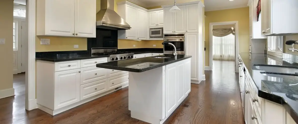 A spacious traditional kitchen with soft yellow walls, white cabinetry, contrasting black granite countertops, and a central island with a prep sink.