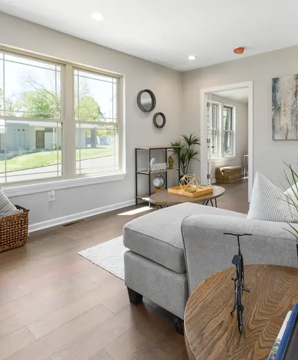 A bright, open-concept living room featuring light gray walls, hardwood flooring, and large windows from a professional home remodeling in La Vista, NE.