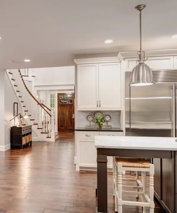 An open concept kitchen remodeling in Papillion, NE, showcasing white cabinets, a marble island, and polished hardwood floors leading to a staircase.