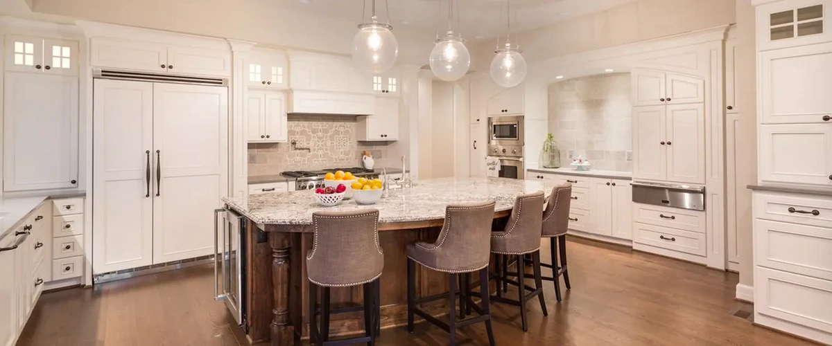 Luxury open-concept kitchen with custom white cabinetry, a large granite-topped center island, and spherical glass pendant lights.