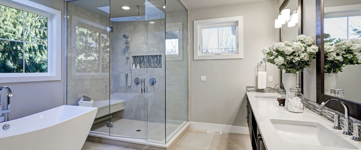 A spacious and bright master bathroom featuring a large glass-enclosed walk-in shower with a built-in bench, a sleek white freestanding soaking tub, and a double vanity with white countertops and floral accents.