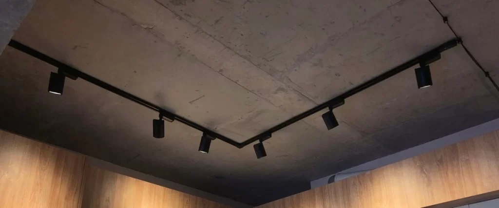 Black industrial-style track lighting with adjustable heads highlighting specific areas of a basement room.