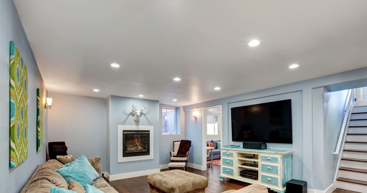 A brightly lit modern basement living room featuring a mix of natural light and warm overhead fixtures.