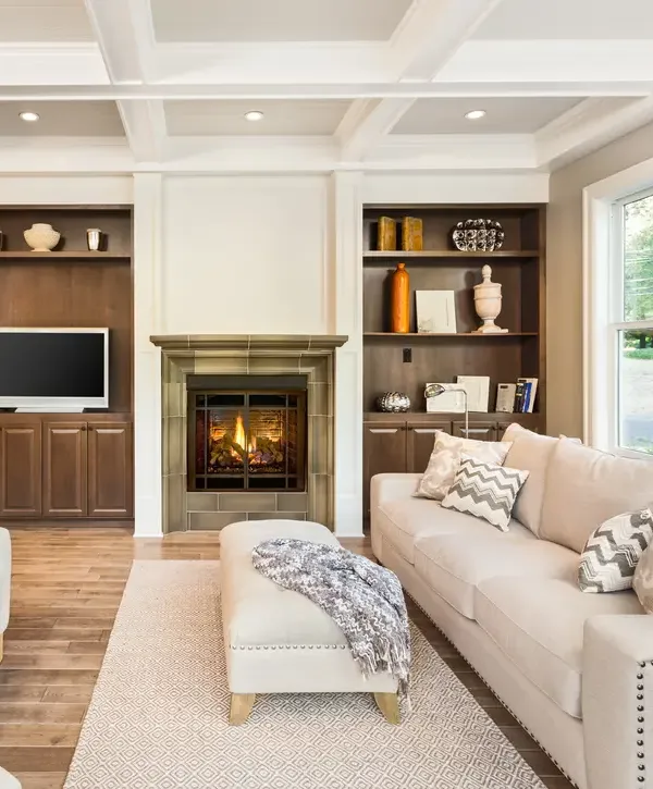 A cozy living room renovation featuring a central fireplace, custom dark wood built-in shelves with a TV, and an elegant white coffered ceiling for a home remodeling project in Bennington, NE.