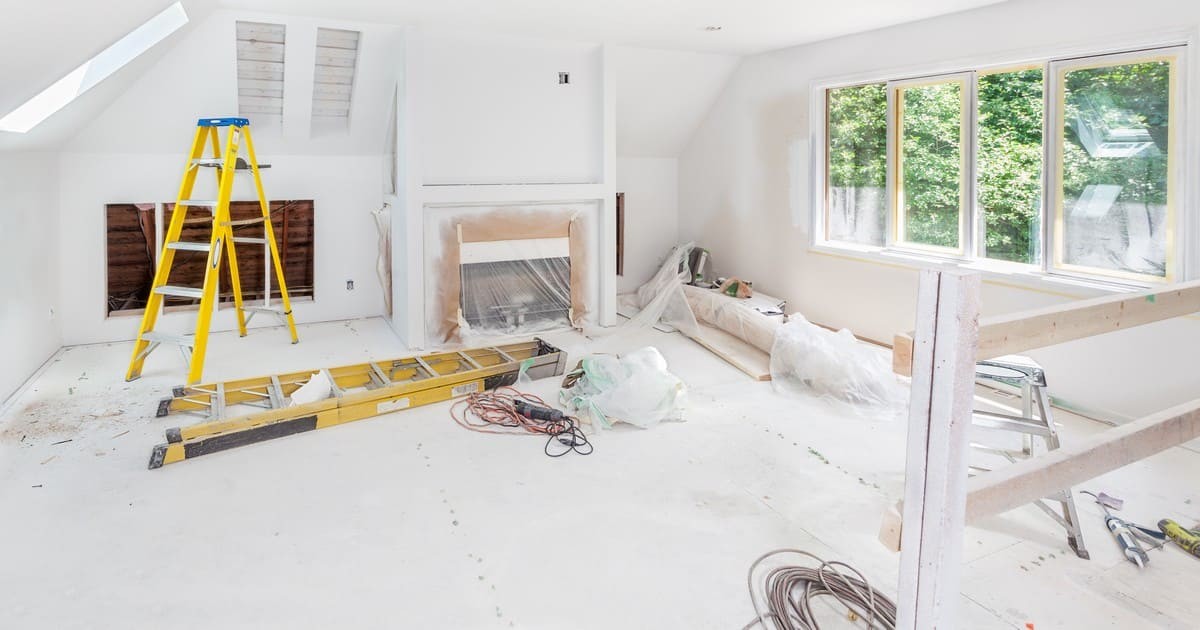 An interior living room undergoing major renovations with yellow ladders, plastic drop cloths, and a covered fireplace, ensuring structural changes meet Omaha building codes.