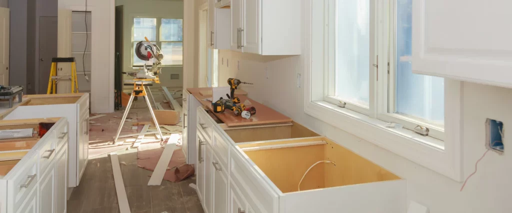An unfinished kitchen remodeling project showing newly installed white base cabinets, a miter saw, and various power tools, highlighting the framing stage subject to Omaha building codes.