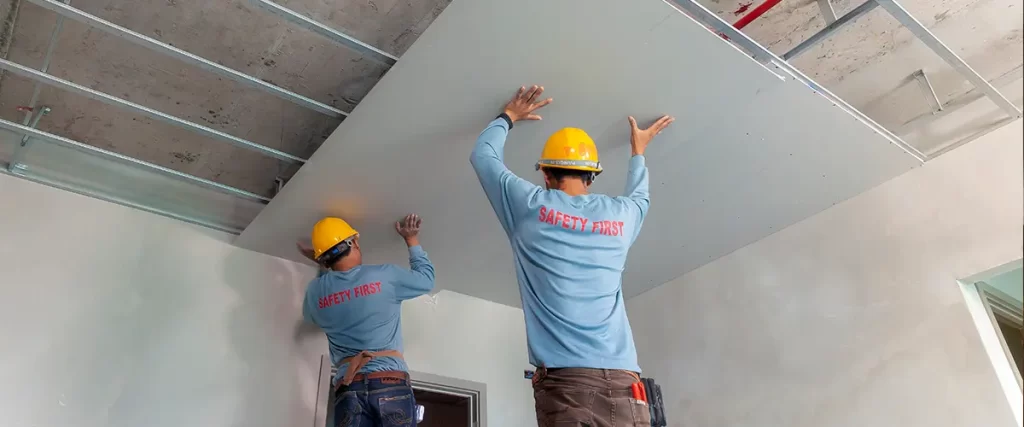 Contractors installing drywall ceiling panels during basement finishing and remodeling project
